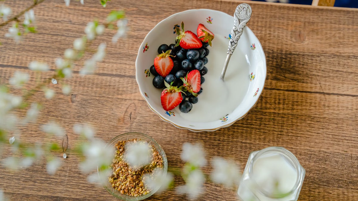 A bowl of fresh strawberries, blueberries with yogurt on a wooden table, viewed from above.